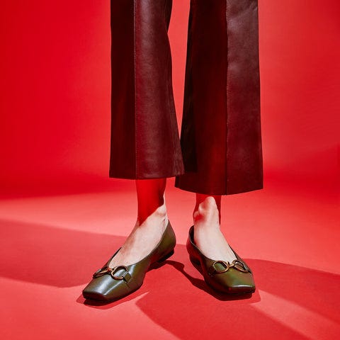 person in green ballet flat shoes against red background