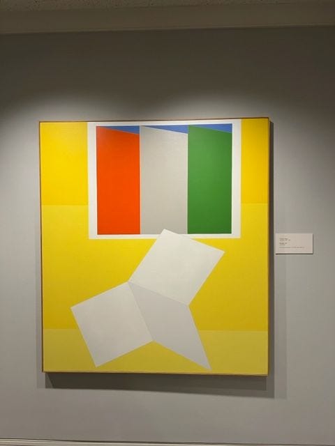 A large abstract painting that with a vibrant yellow background. In the center, a large white shape that resembles a paper airplane is prominant. Surrounding it are panels of red, grey, and green with a strip of blue along the top.