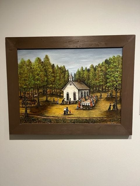 A painting of a small white church in the woods. There are people outside of the church seated at a table and gathering outdoors.