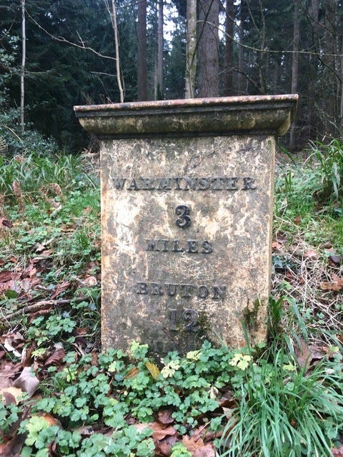 Milestone in a forest showing Warminster 3 miles and Bruton 12 miles.