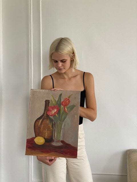 Peurrung stands holding the painting; it is of a vase of flowers in front of a larger, brown vase.