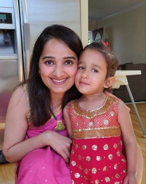 Neha stands in her kitchen next to her adorable daughter!