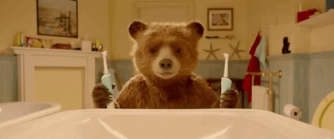 A gif of a bear using two electric toothbrushes to clean it ears, nose and teeth; scene from movie ‘Paddington’