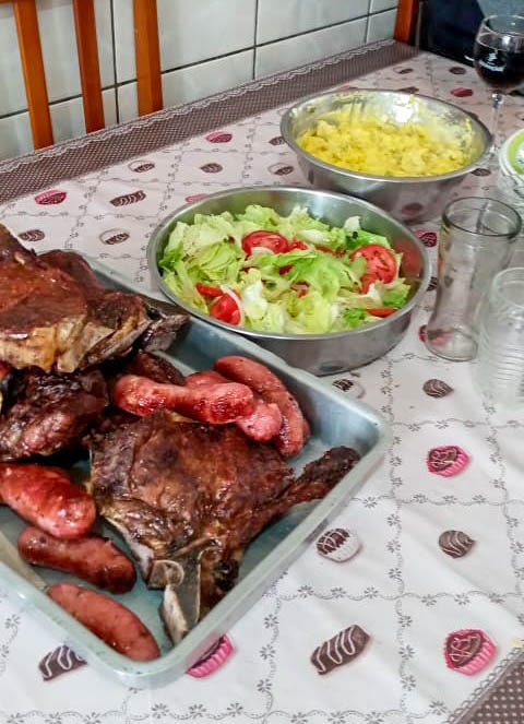 Mesa servida de churrasco, salada de folhas e salada de batata com maionese.