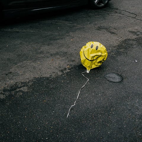 A smiling yellow emoji balloon on the ground during the daytime