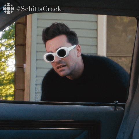 David Rose of ‘Schitt’s Creek’ wearing white feminine glasses as he leans into a car’s passenger-side window asking “What? Why? Why?”