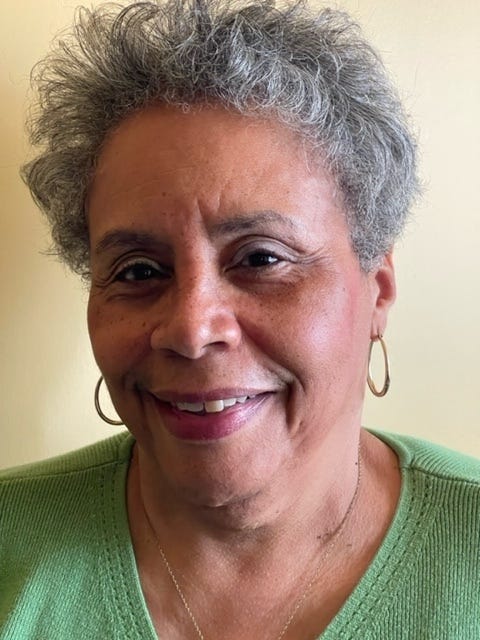 A Black woman with short gray hair wearing a green shirt and gold hoops smiles for a picture