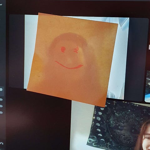 A Post-it with a smiley drawn on it stuck on the screen, over someone’s face, during a video call.