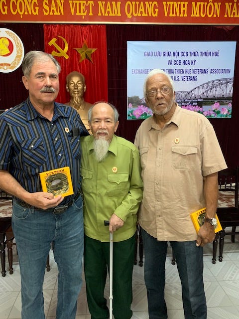 Two U.S. veterans stand on either side of a Vietnamese veteran.