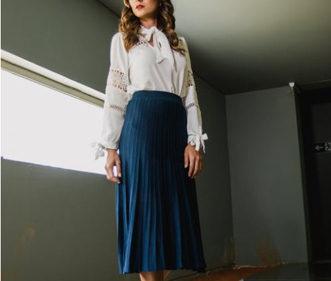 Woman dressed in blue pleated skirt and white blouse