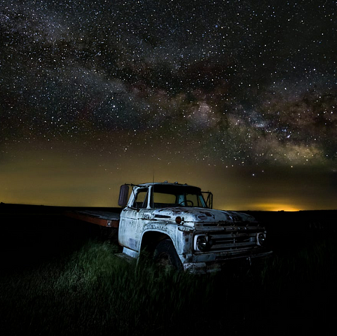 Old rusted-out truck in a black field under a starry sky.