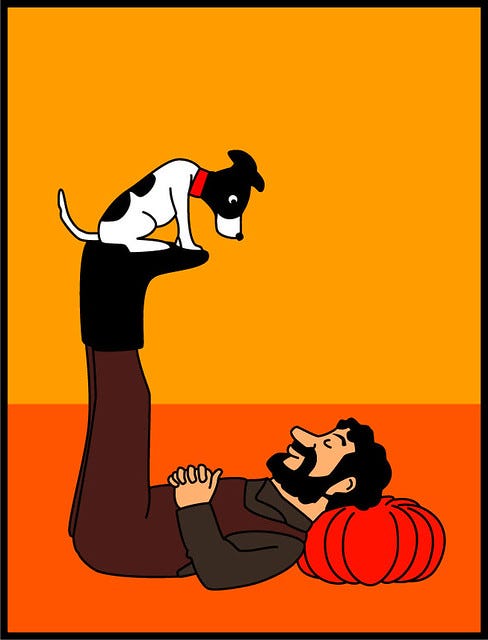 A bearded person lying on their back, with their eyes closed, balances a small dog on their feet. The dog looks at them.