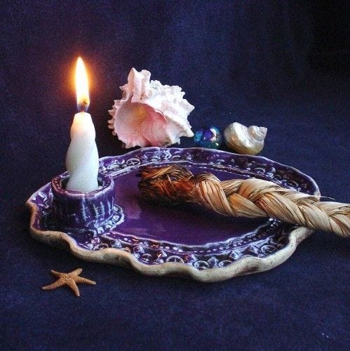 A simple altar with a candle, burning incense, and a few seashells.