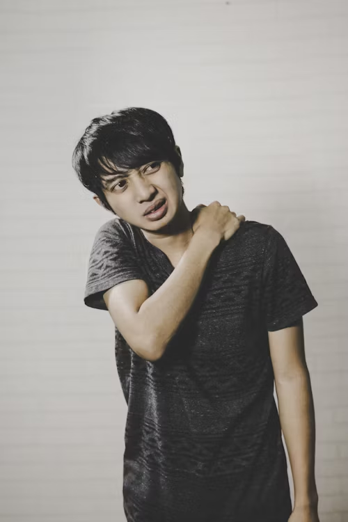 A young man winces while grabbing his trapezius muscle