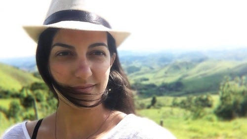 Fotografia do rosto da Leila. Ela usa chapéu branco e, ao fundo, estão montanhas.