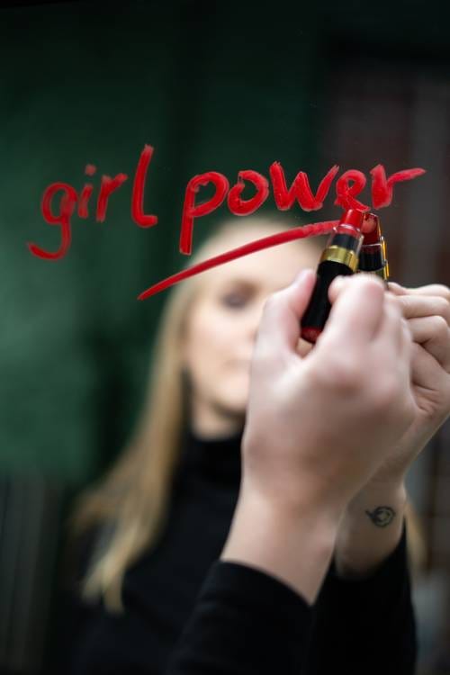 A woman writing “girl power” on a mirror in lipstick