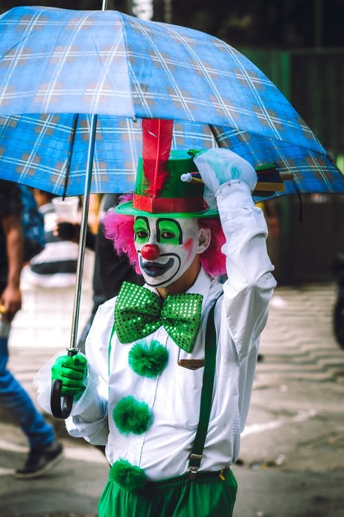 A clown poses underneath his blue umbrella