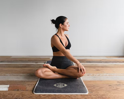 A woman sitting on a yoga mat performing a stretch with her legs crossed and her arm extended across her body