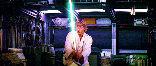 Luke Skywalker treinando com seu sabre de luz enquanto uma bola, uma espécie de robô, solta tiros de luz.