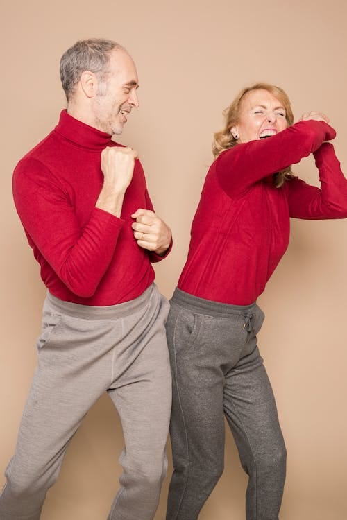 Cheerful mature couple dancing and laughing against beige background