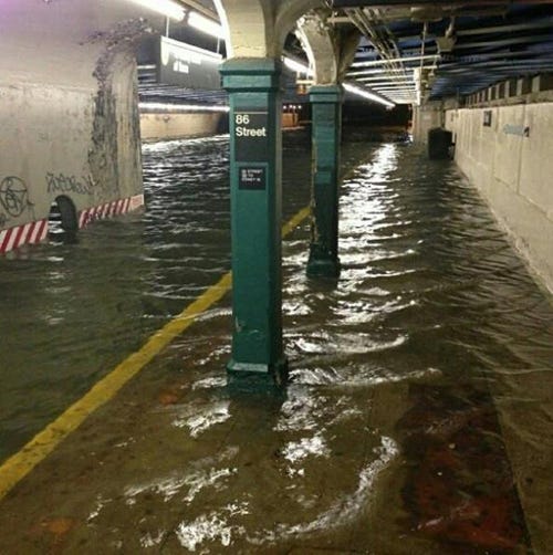 A photograph of the New York City Subway flooded by storm surge waters. The entire subway is in waste high water.