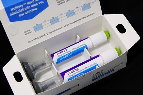 A publicity photograph of Eli Lilly’s Trulicity therapy. Two white self-injection pens lie side-by-side in a cardboard carton