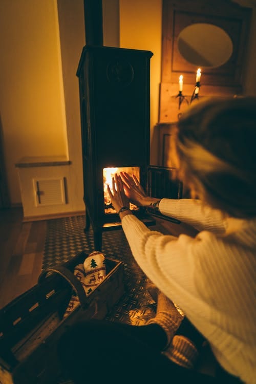 Girl sits by the fireplace warming her hands