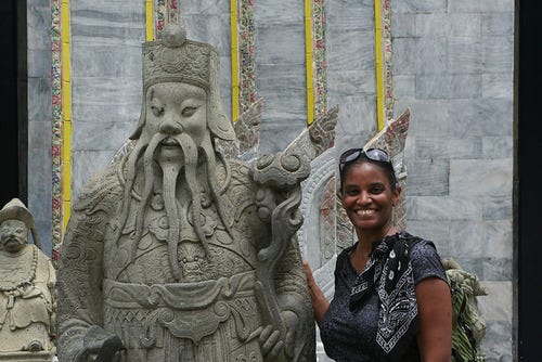 A photo of Michelle Harris standing next to an ancient statue at Wat Phra Kaeo in Bankok, Thailand