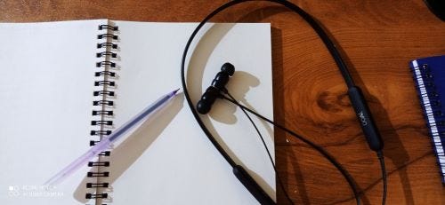 A wireless neckband on table with pen and notebook.