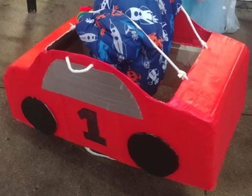 Red race car costume made from cardboard boxes with silver duct tape windows and painted wheels with the number 1 on the side