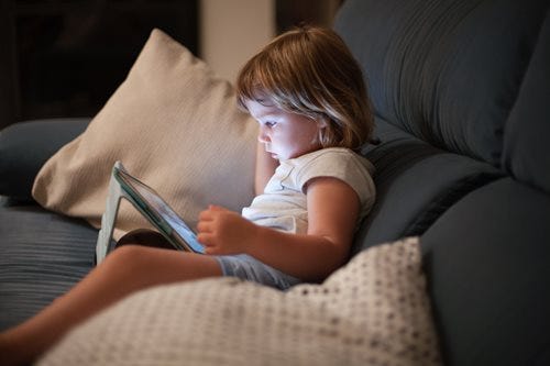 Young short-haired blonde girl sitting on couch with tablet lighting up her face