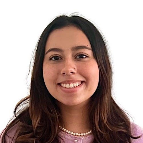 Photo of Natalia, a slightly tan Latina woman with medium length dark brown hair. She is smiling with her teeth and her hair is in front of her shoulders. She is wearing a lavender long sleeve top with a pearl necklace.