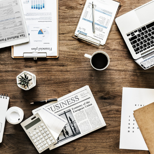 IMAGE OF BUSNESS NEWS PAPER, A LAPTOP, CUP OF TEA AND A CALCULATOR ON WOODEN BROWN TABLE