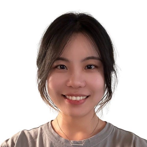 Photo of Janet, an Asian woman, from the shoulders up. She is looking at the camera with an open-lipped smile. She is wearing a grey top with a necklace.