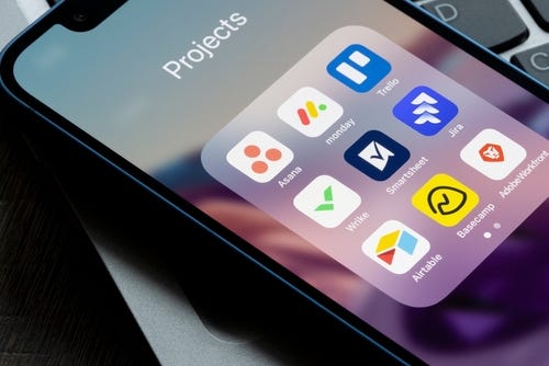 Assorted apps for project management are seen on an iPhone, including Asana, Monday, Trello, Wrike, Smartsheet, Jira, Airtable, Basecamp, and Adobe Workfront.