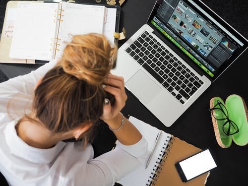 A woman at a desk with a laptop and stressed out