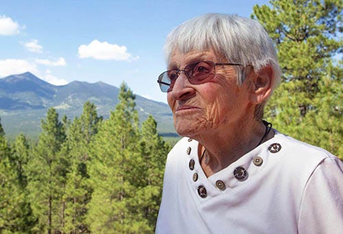 Photo of an elderly Carolyn Shoemaker standing in front of trees and a mountain