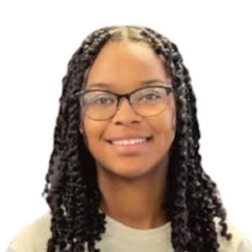 Photo of Roshanell, a Black woman from shoulder up. She is looking at the camera with an open lipped smile. She is wearing a white shirt. Her black hair is in twists, and it is shoulder-length.