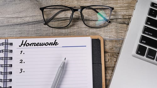 Image of reading glasses, the side of a laptop and a notepad with the word ‘Homework’ at the top.