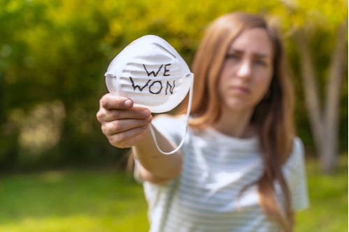 A woman holding up a face mask with the words “WE WON” written on it