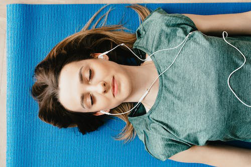 Woman listening to music while lying down on a blue yoga mat