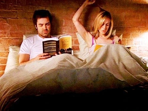 Berger and Carrie sitting in bed reading, while Carrie pulls on her hair and Berger sighs.