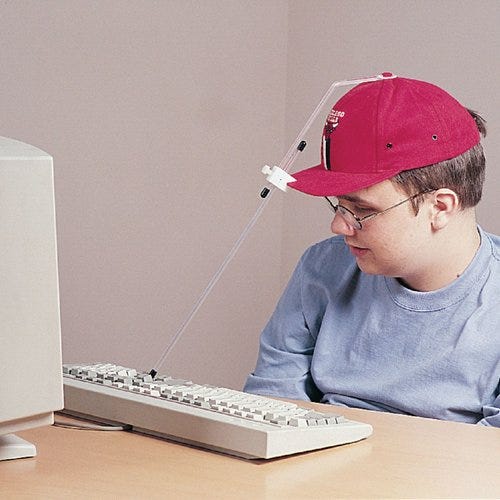 A person with a motor impairment using a baseball cap with a head pointer to type on his computer’s keyboard.