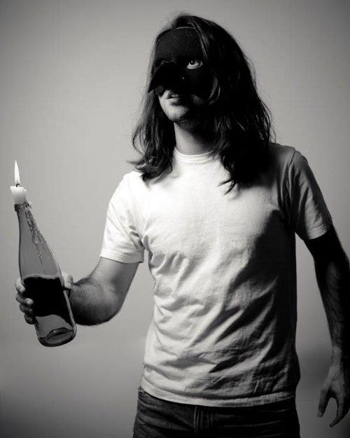 A self-portrait of Márcio Faustino Santos weating a mask and holding a bottler with a lighted candle on it.