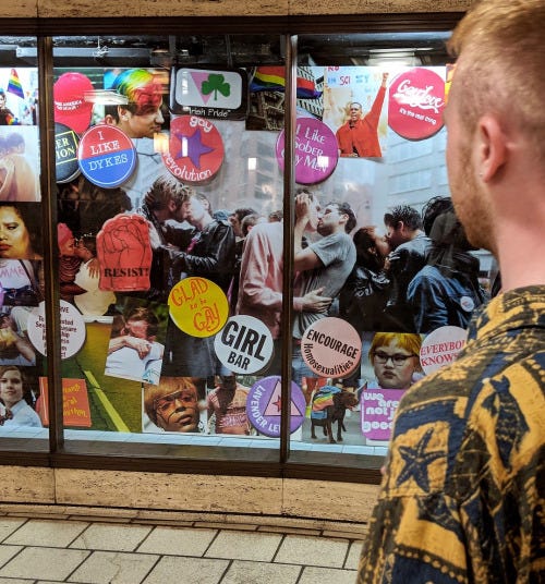 A window display featuring a collage of imagery of Pride protests, covered with historic pins, badges and pictures of faces.
