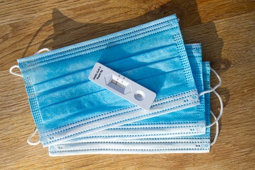 A pile of blue and white disposable face masks on a table with a negative covid lateral flow test on top.