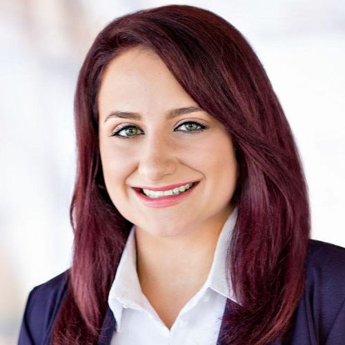 Woman with red hair, a white shirt, and black blazer smiling.