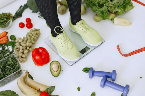 A person standing on a bathroom scale with veggies around