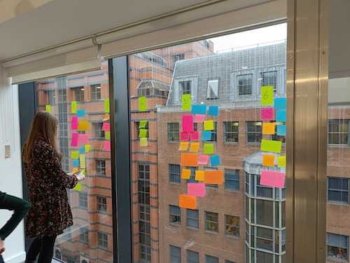 A woman stands at a window that is covered in colourful post-it notes