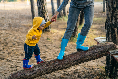 Little kid balancing on a fallen tree trunk with a help of an adult